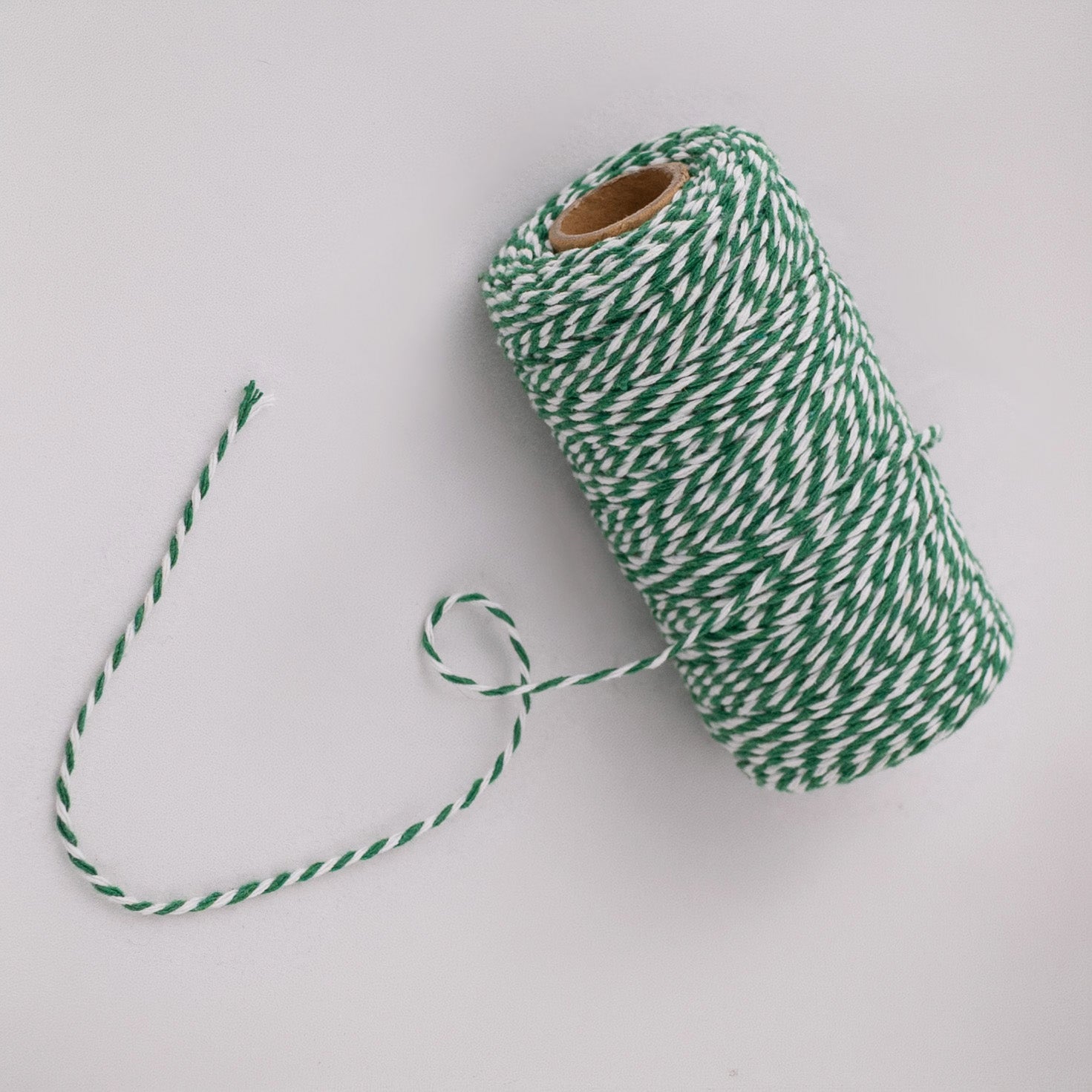 Roll of green and white striped butcher string, butcher twine, meat string, meat twine on a light gray background