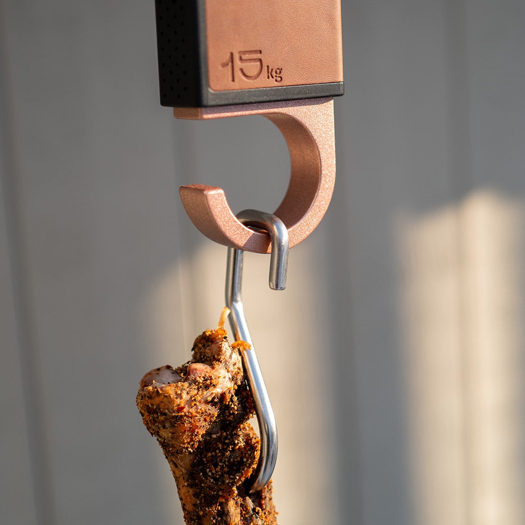 Meatdryer hook with a ham hanging on a food safe sharp stainless steel metal meat hook on a gray background
