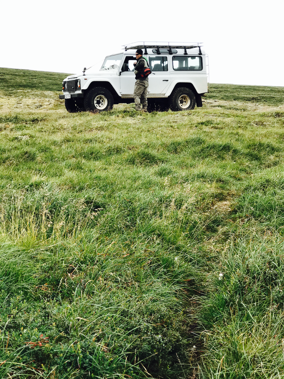 Person standing next to a white off-road vehicle Land Rover in a grassy field