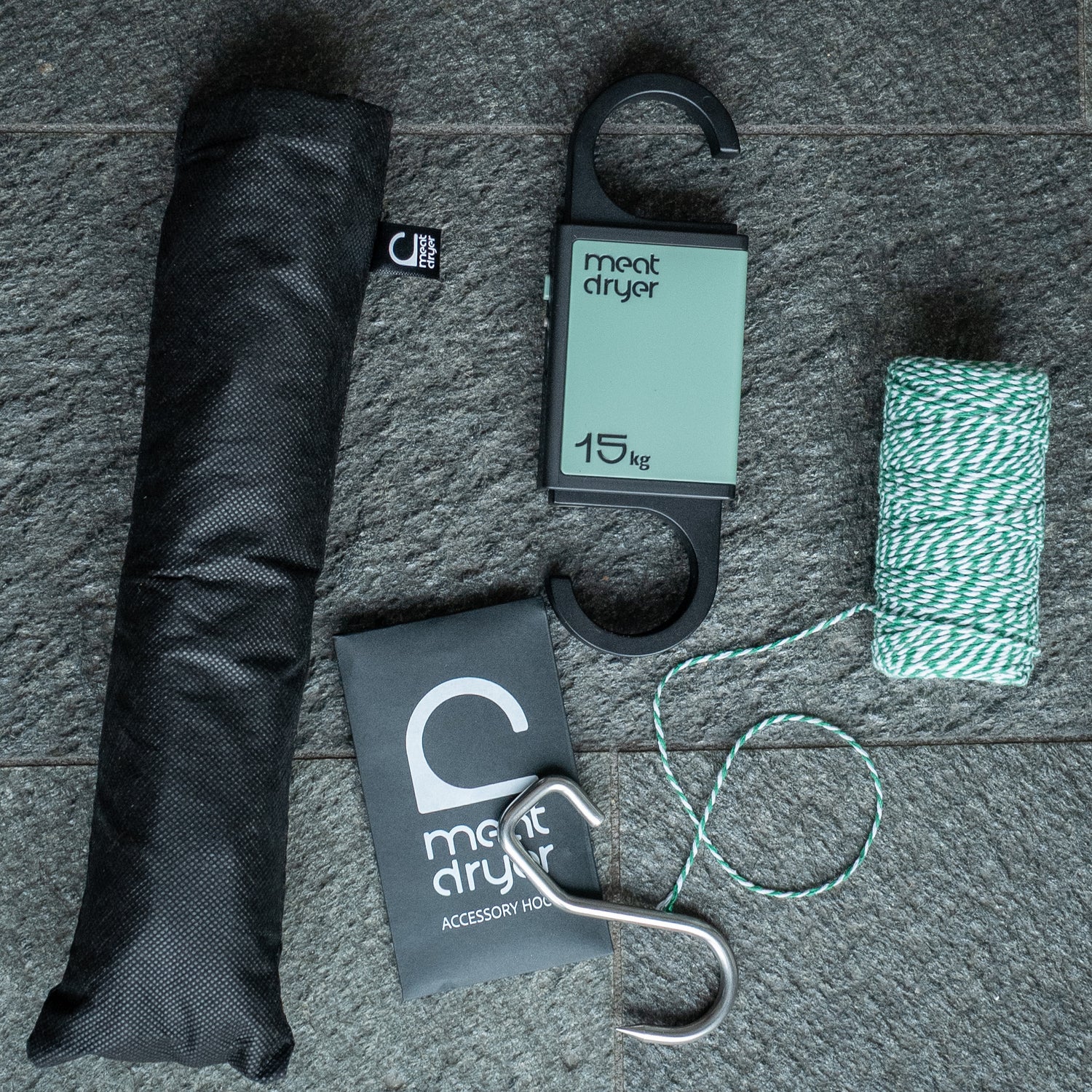 Meat drying equipment including a black insect net, string, and sharp metal meat hook on a stone surface