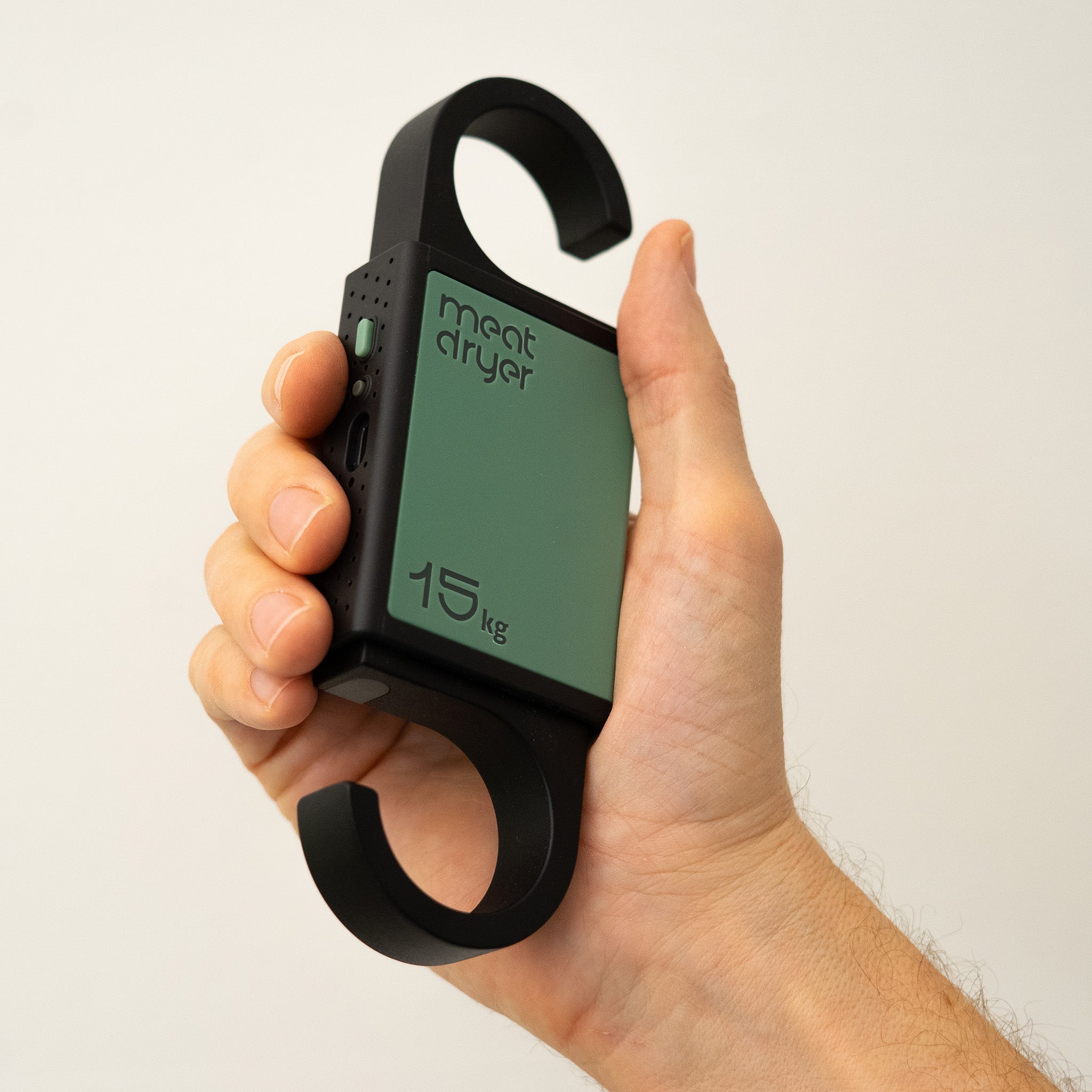 Hand holding a black and green meatdryer hook against a white background