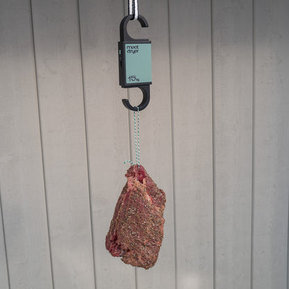 Biltong beef meat hanging from a green Meatdryer hook with a weight , temperature and humidity indicator against a grey background