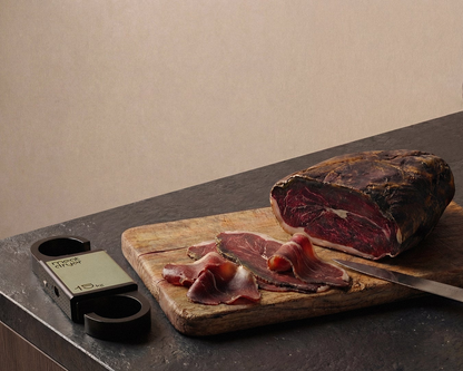Sliced cured meat on a wooden cutting board with a meatdryer digital thermometer,  humidity meater and smart weight scale on a dark surface.